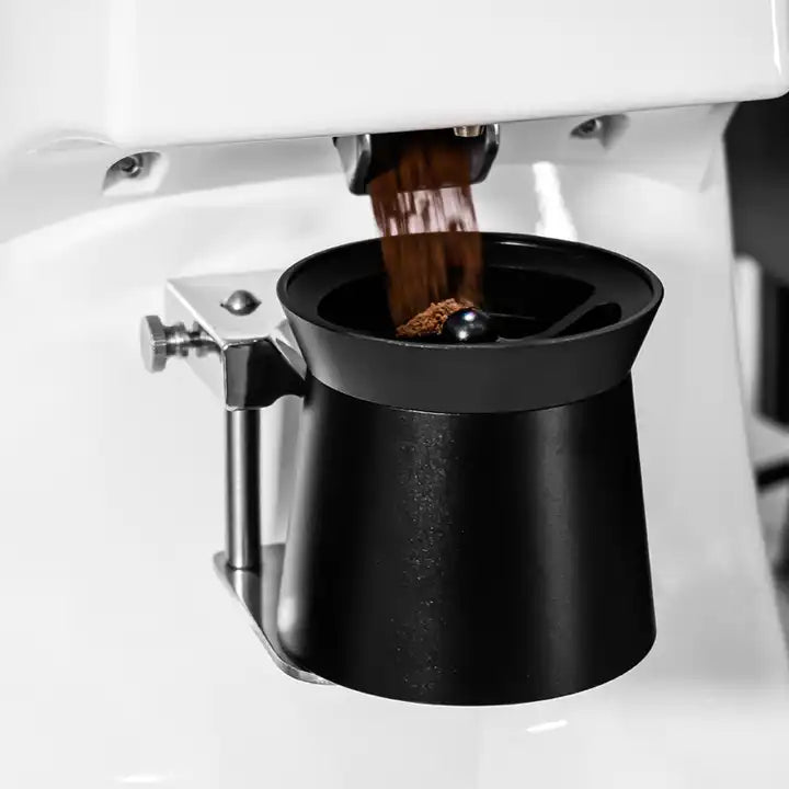 Abbildung des Brewout Distribution-Dosierbechers in schwarz mit Echtholzabdeckung eingehängt in eine weiße, elektrische Espresso-Mühle während des Mahlvorgangs. Das Produkt dient als Kombination aus WDT Tool, Dosierring und Mahl-Behälter. 